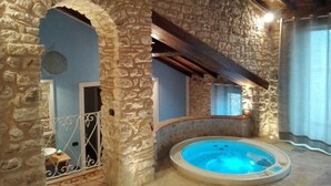 A stone-walled room with a hot tub, a balcony with a metal railing, and a wooden ceiling. - Locanda Il Falco Nero (Fumone)