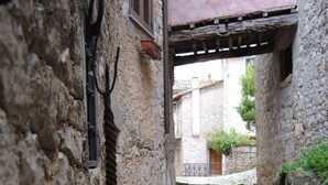A narrow stone pathway flanked by rustic stone walls, leading to a building with a pink facade and a wooden balcony. - Locanda Il Falco Nero (Fumone)