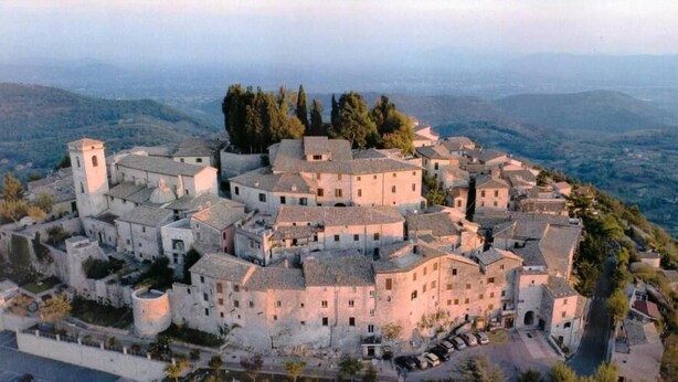 A historic walled town with a central tower, surrounded by buildings with uniform architecture, set against a mountainous backdrop. - Locanda Il Falco Nero (Fumone)