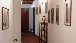 A hallway with framed pictures on the walls, a wooden chair, and a door at the end. - Locanda Il Falco Nero (Fumone)