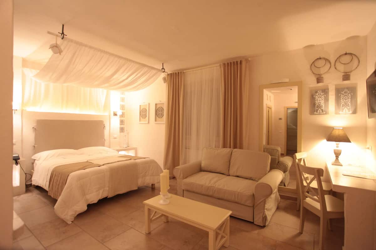 A hotel room with two beds, a sofa, a desk, and a bedside table.