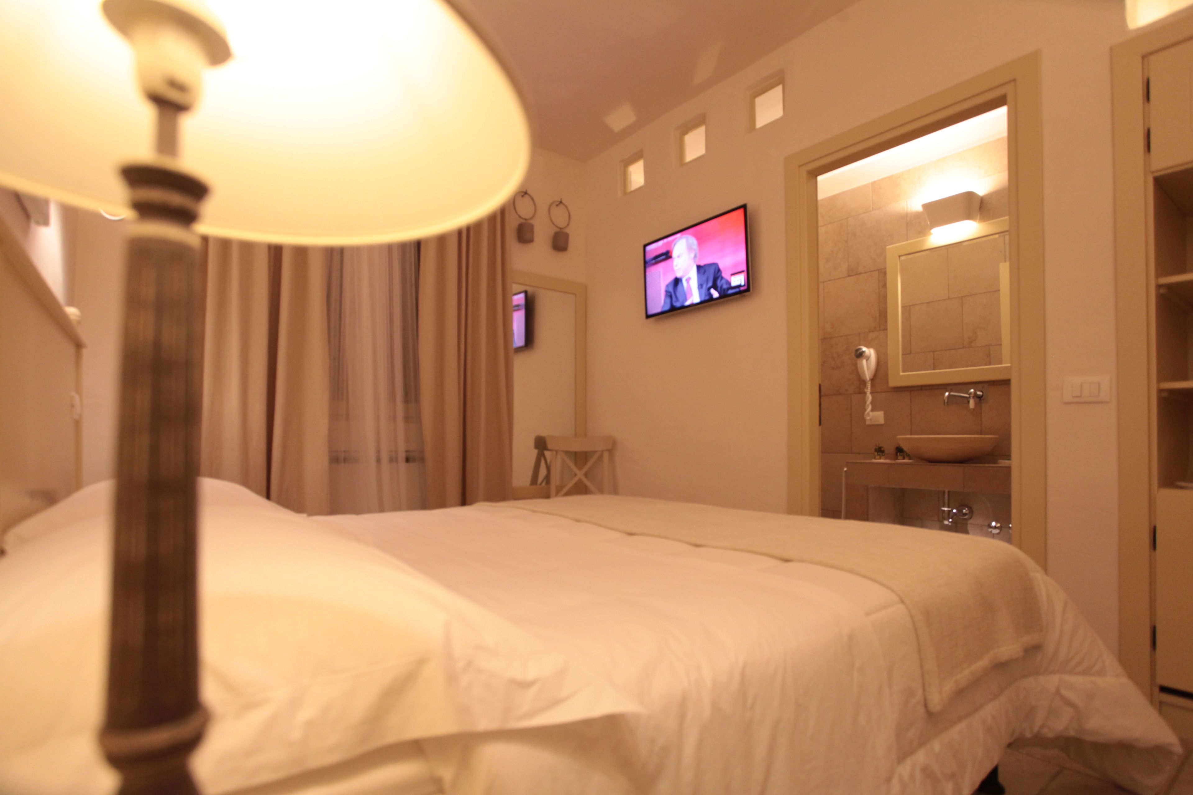 Habitación de hotel con cama, televisión, baño con lavabo y espejo, y una lámpara.