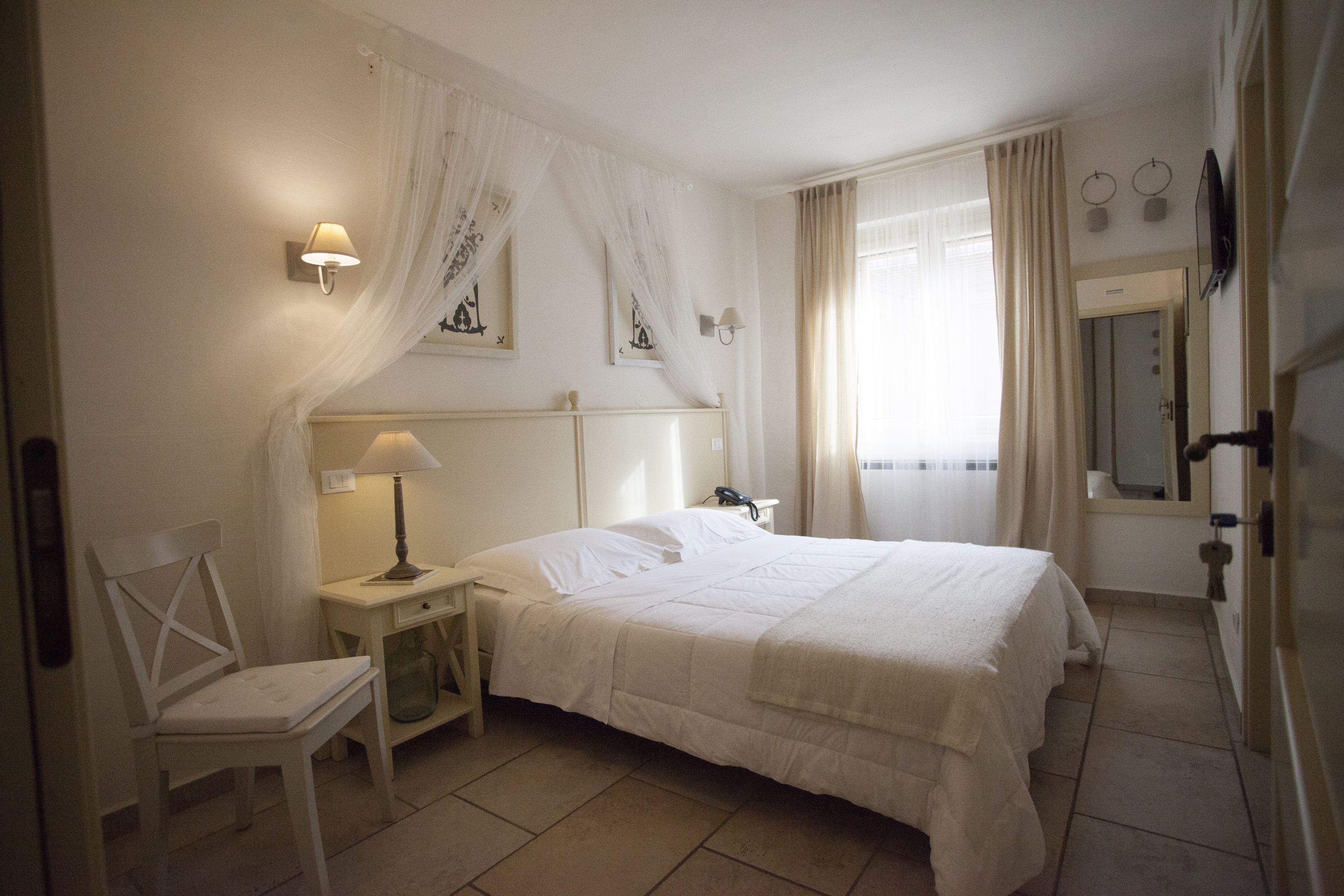 Een hotelkamer met een bed, een stoel, een nachtkastje, een lamp, een spiegel en gordijnen.