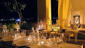 Mesa dispuesta para cenar, con velas, copas y botellas, con vista a un paisaje urbano nocturno.