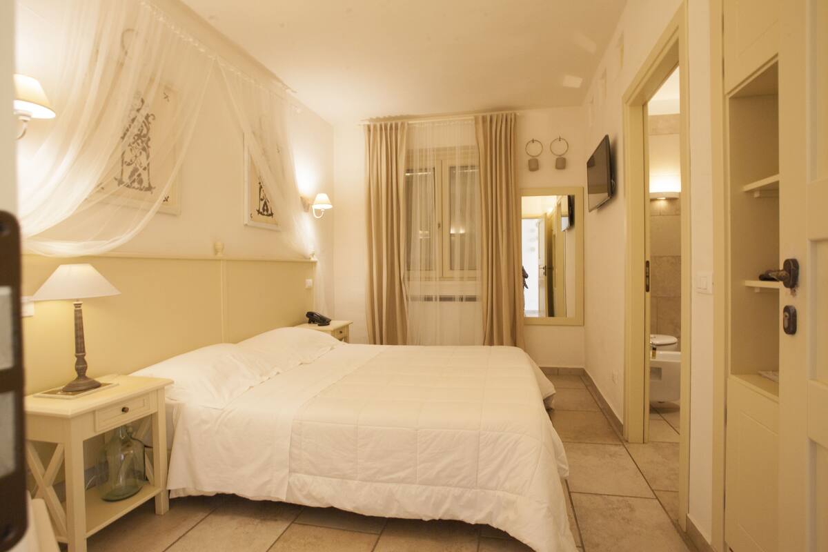 A hotel room with a bed, bedside table, lamp, curtains, and a television on the wall.
