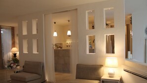 Una sala de estar con dos sofás, una mesita de noche con una lámpara y una pequeña mesa con otra lámpara. Hay un espejo en la pared y una ventana con cortinas.