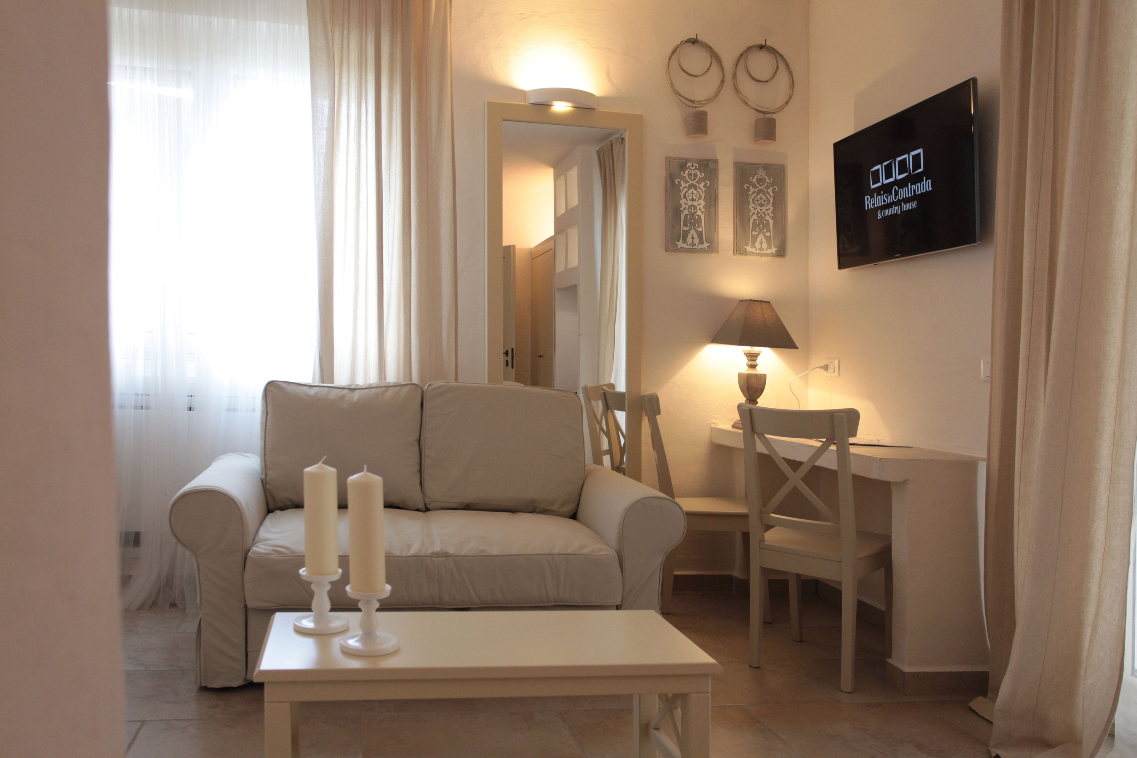 A living room with a sofa, a table with candles, a TV mounted on the wall, and a lamp.