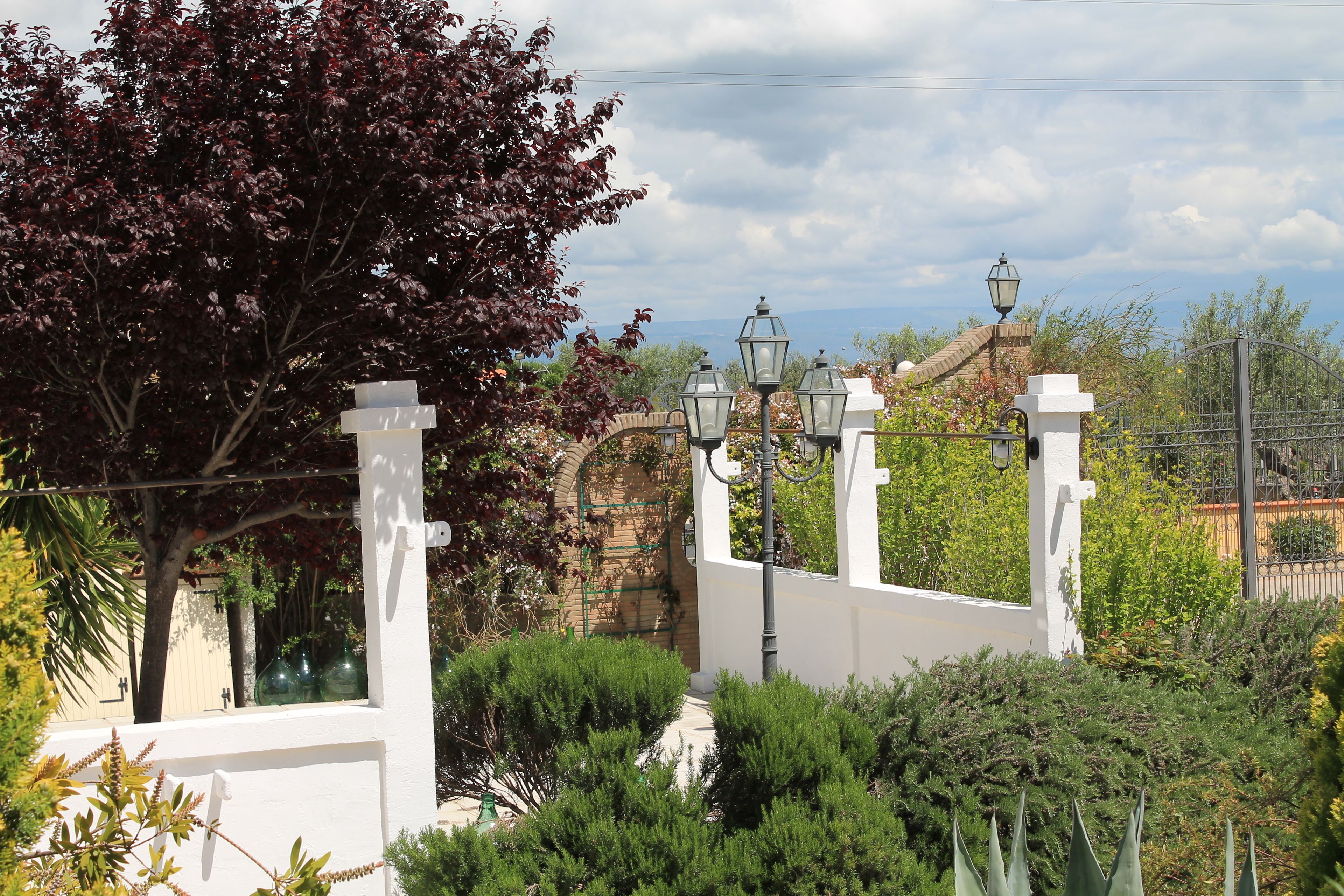 A white wall with a metal gate, a tree with red leaves, and a street lamp.