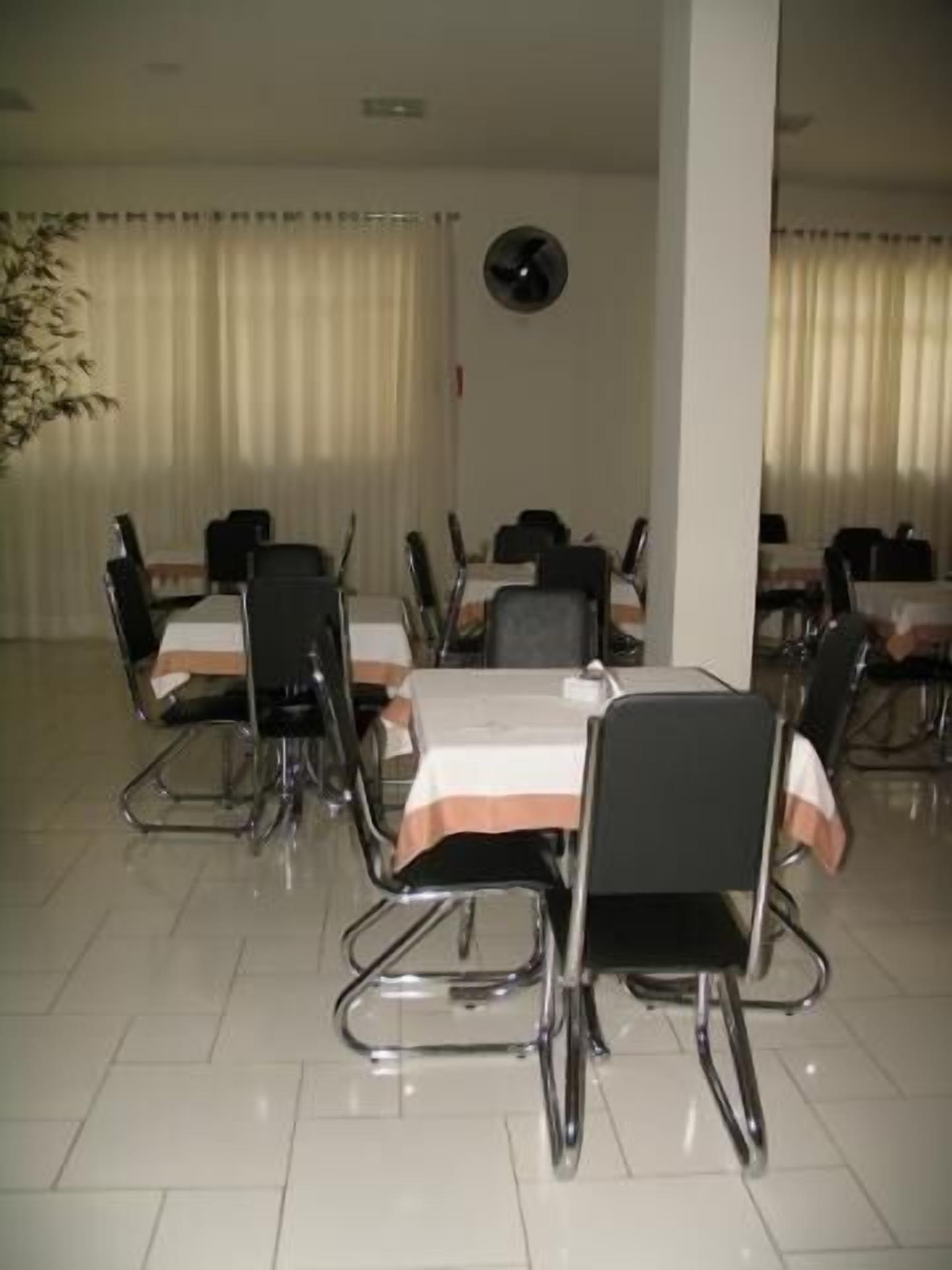 A dining area with tables and chairs, a clock on the wall, and curtains on the windows.