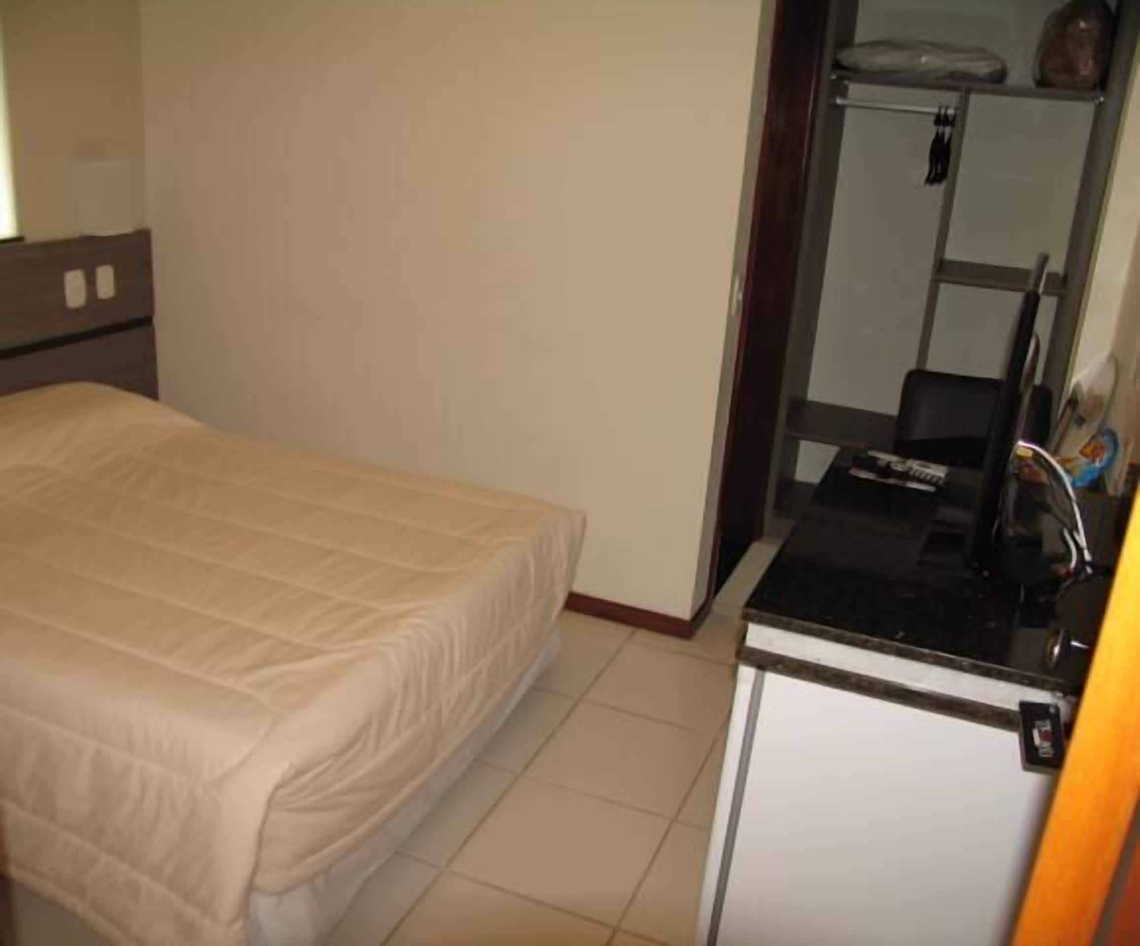 A small, clean room with a bed, a kitchenette, and a mirror.
