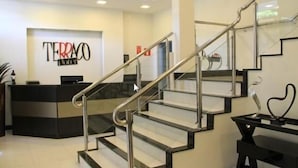 A reception area with a staircase, a reception desk, and a wall-mounted sign. - Terraço Hotel (Tres Pontas)