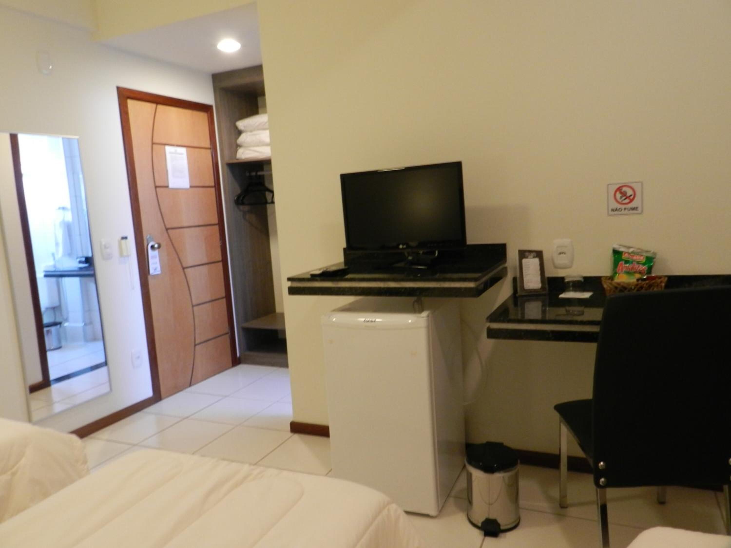 Habitación de hotel con cama, escritorio con computadora, refrigerador, basurero y una silla.