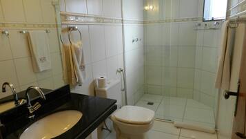 Casa de banho com lavatório em bancada preta, sanita branca e zona de duche com vedação de vidro.