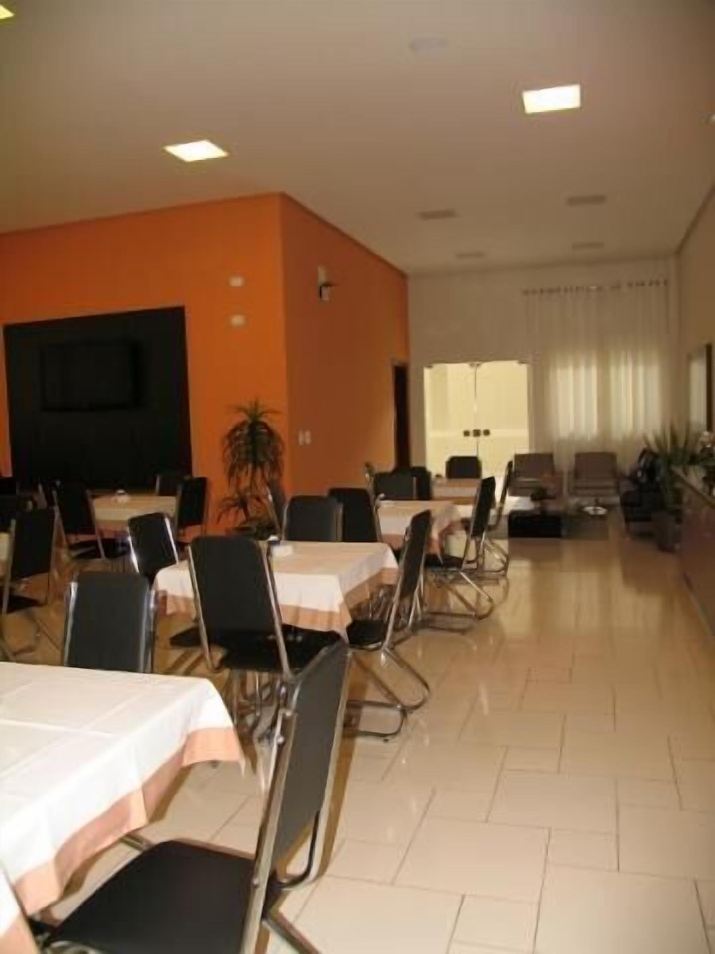 Un salón de conferencias con mesas, sillas, un televisor y una ventana con cortinas.