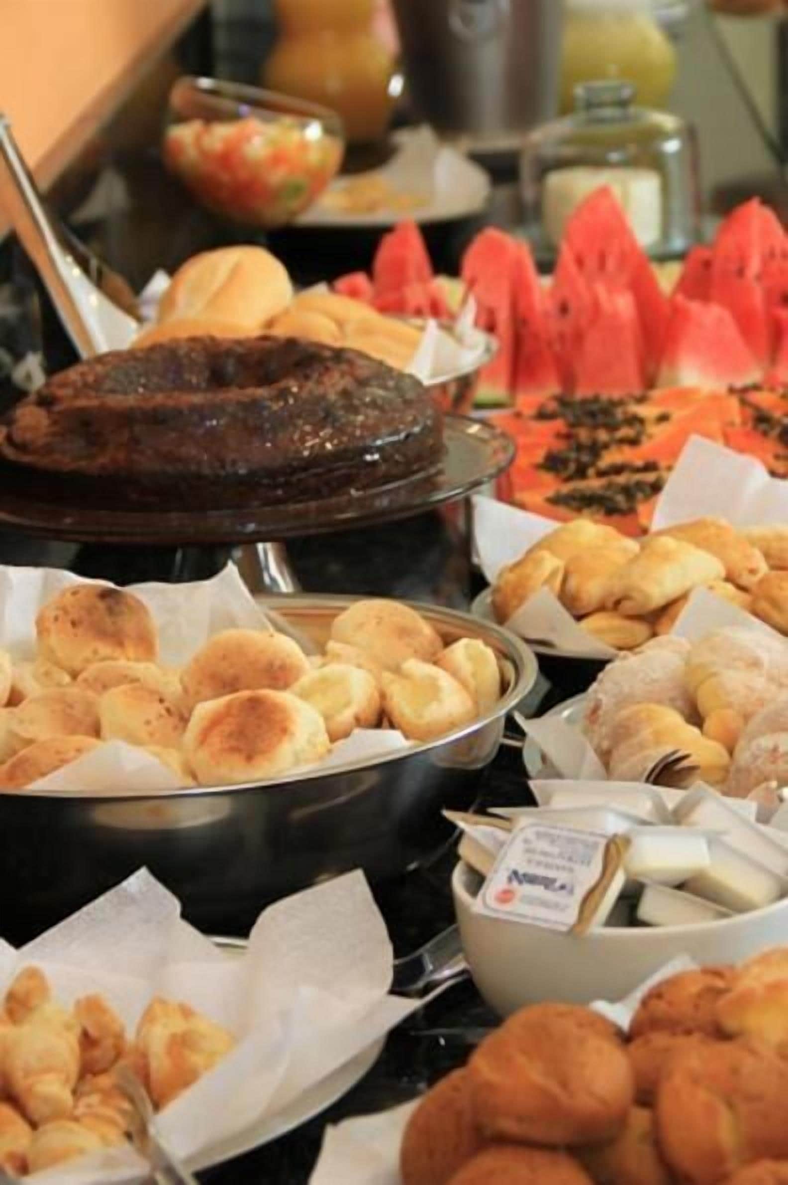Un bufé con diversos alimentos, incluyendo un gran plato de carne, pasteles y sandía en rodajas.