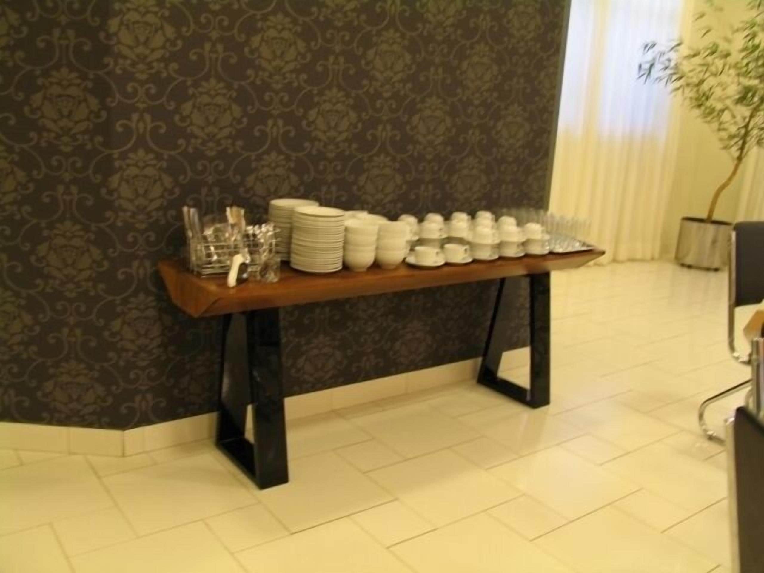 A table with stacked plates, bowls, and glasses against a patterned wall.