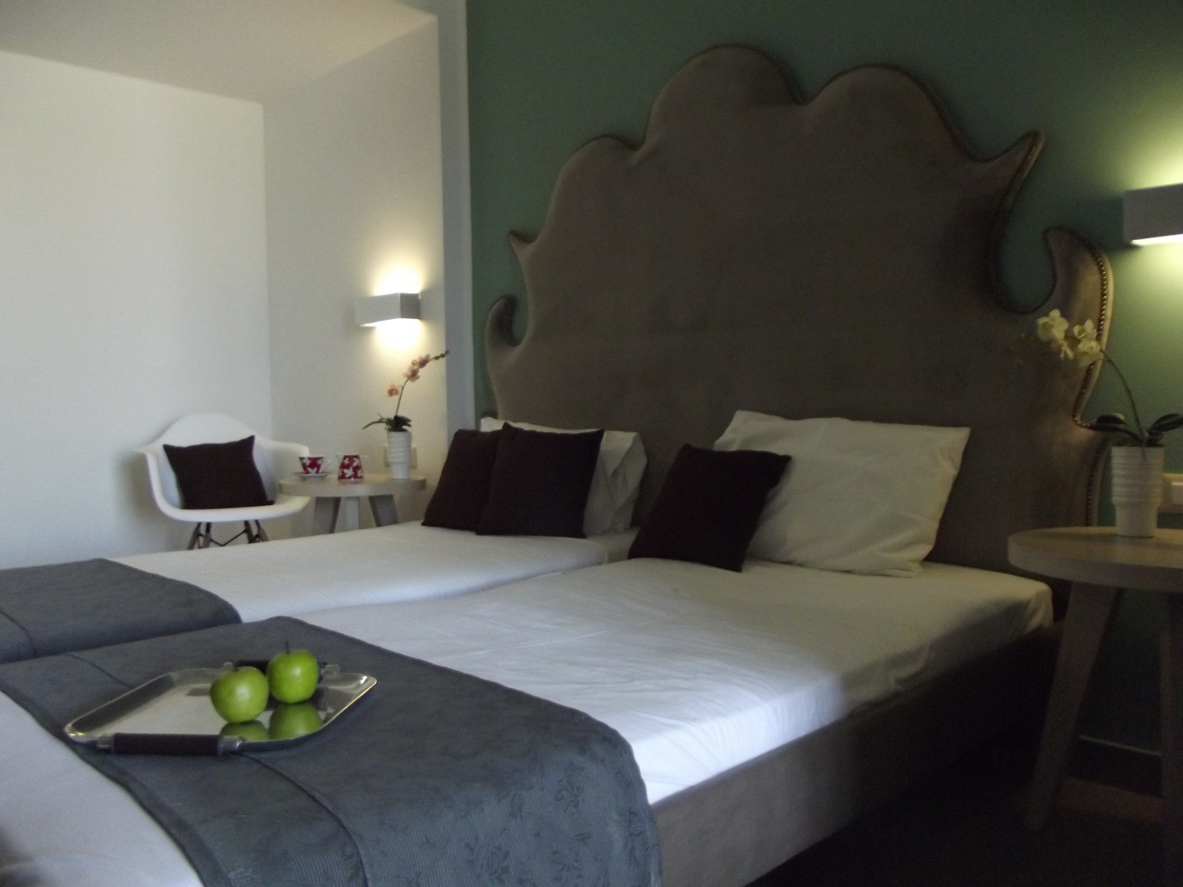 A hotel room with a large bed, a bedside table with a lamp, a chair, and a small table with a plant.