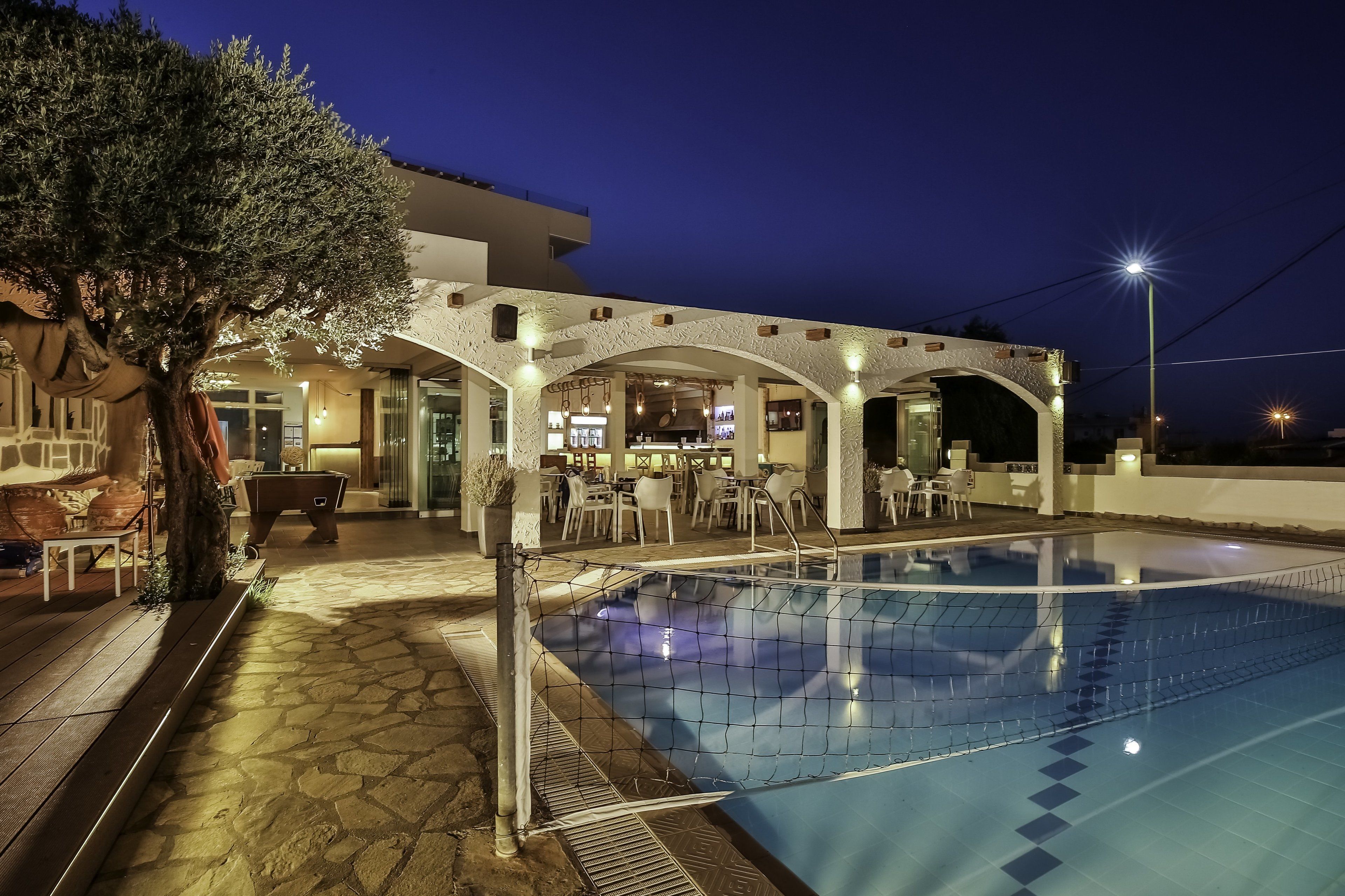 A swimming pool with a stone deck, a bar area with outdoor seating, and a large tree.