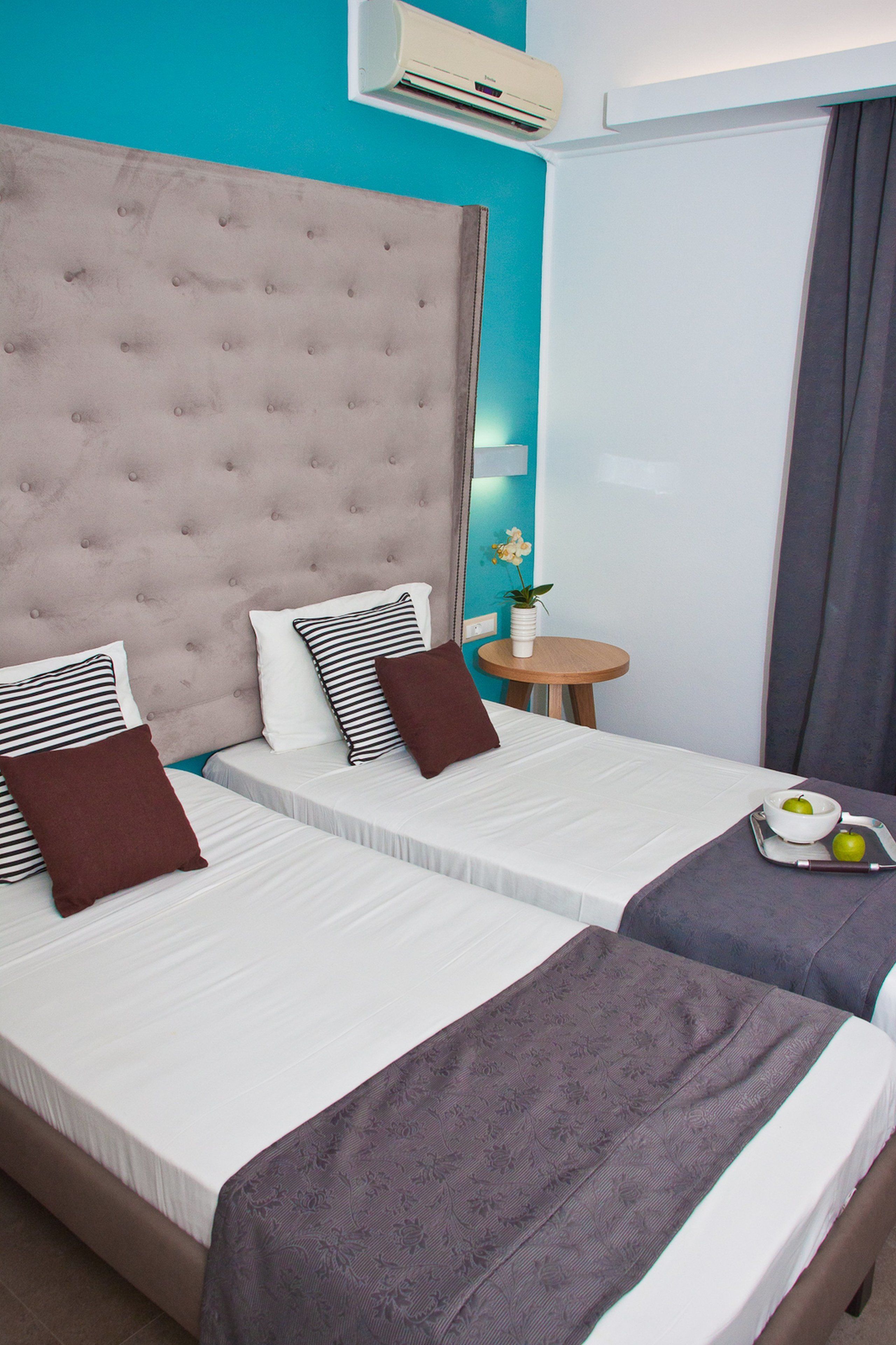 A hotel room with two beds, a round wooden table, a small potted plant, and a tray with apples and a bowl.