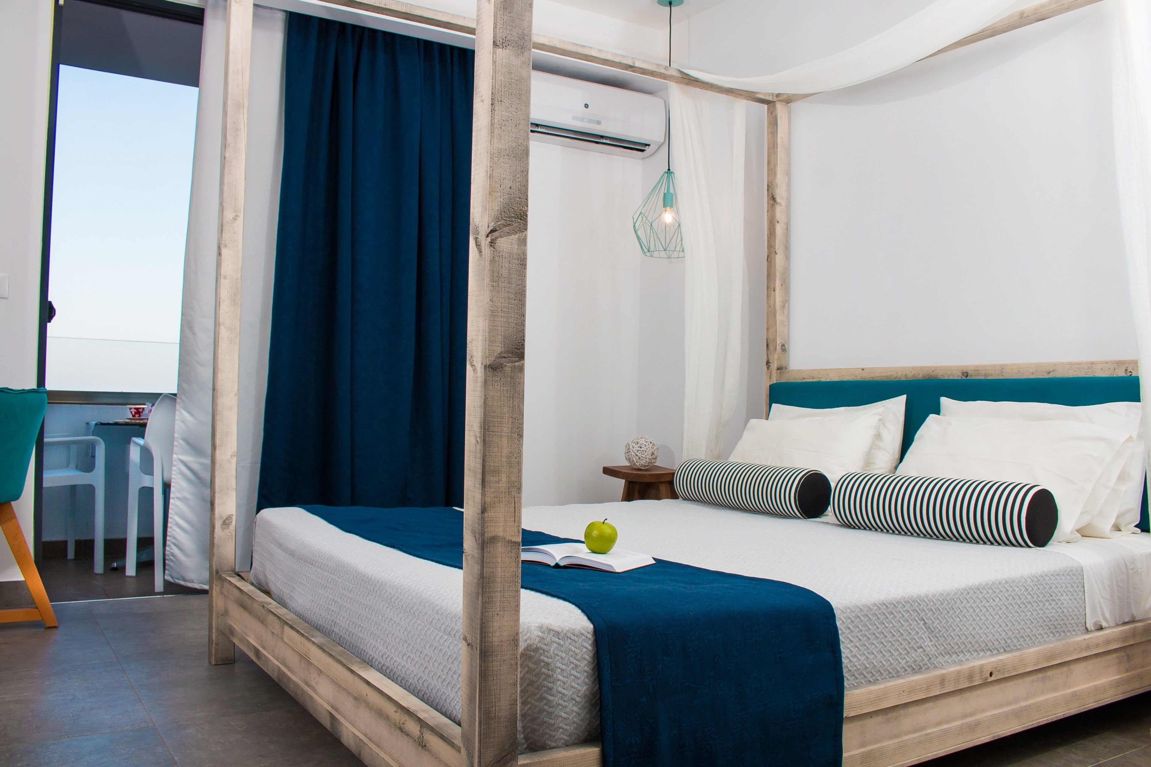 A room with a wooden four-poster bed, a desk with a chair, and a view through an open door.