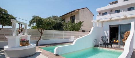Une piscine avec une terrasse blanche, un mur blanc et un bâtiment en arrière-plan.