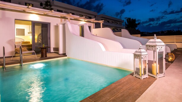 Une piscine dotée d’une terrasse blanche et d’une structure en verre, entourée d’un bâtiment moderne avec des balcons.