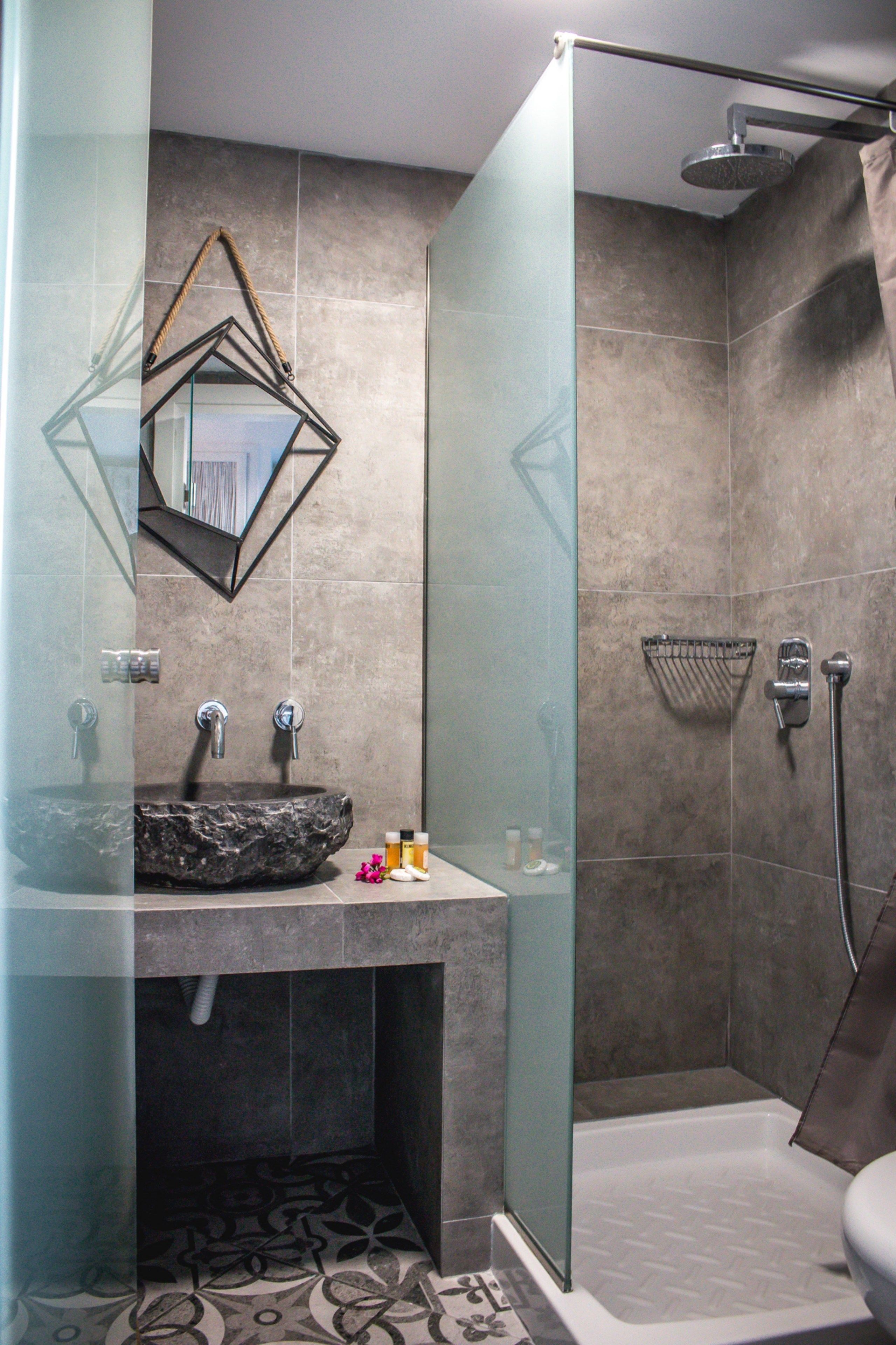 A modern bathroom with a glass-enclosed shower, a marble sink, and a geometric mirror.