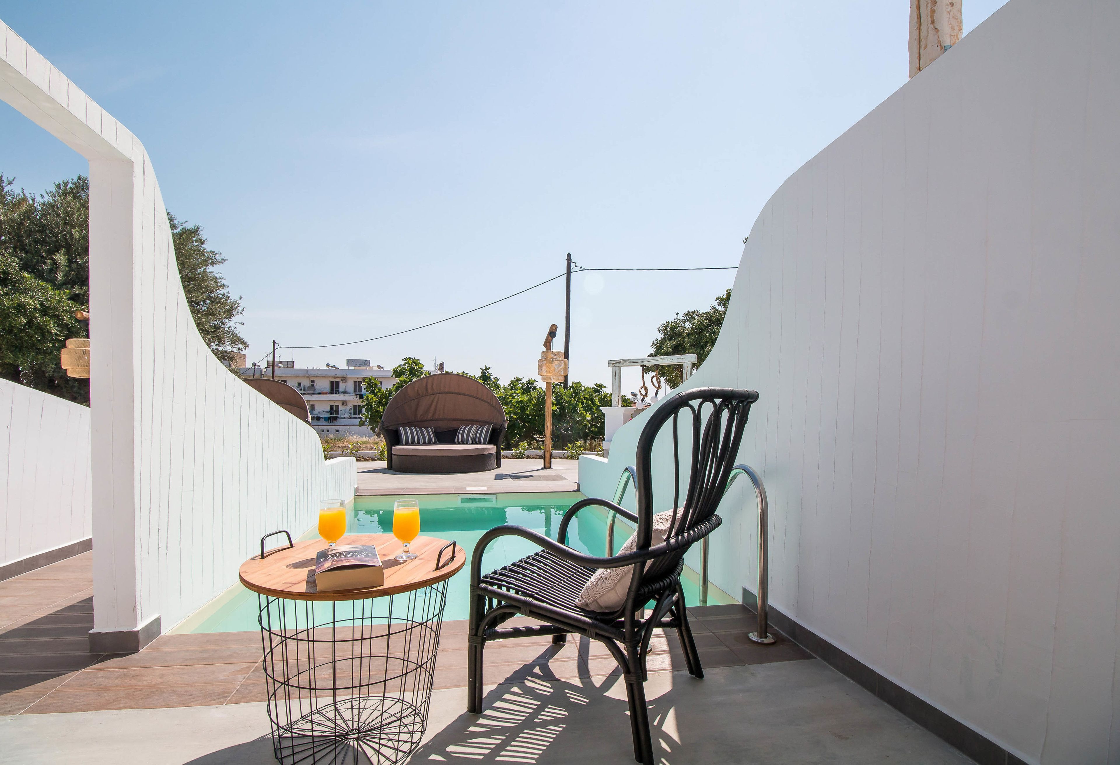 A poolside area with a round table, a wicker chair, and a glass of orange juice.