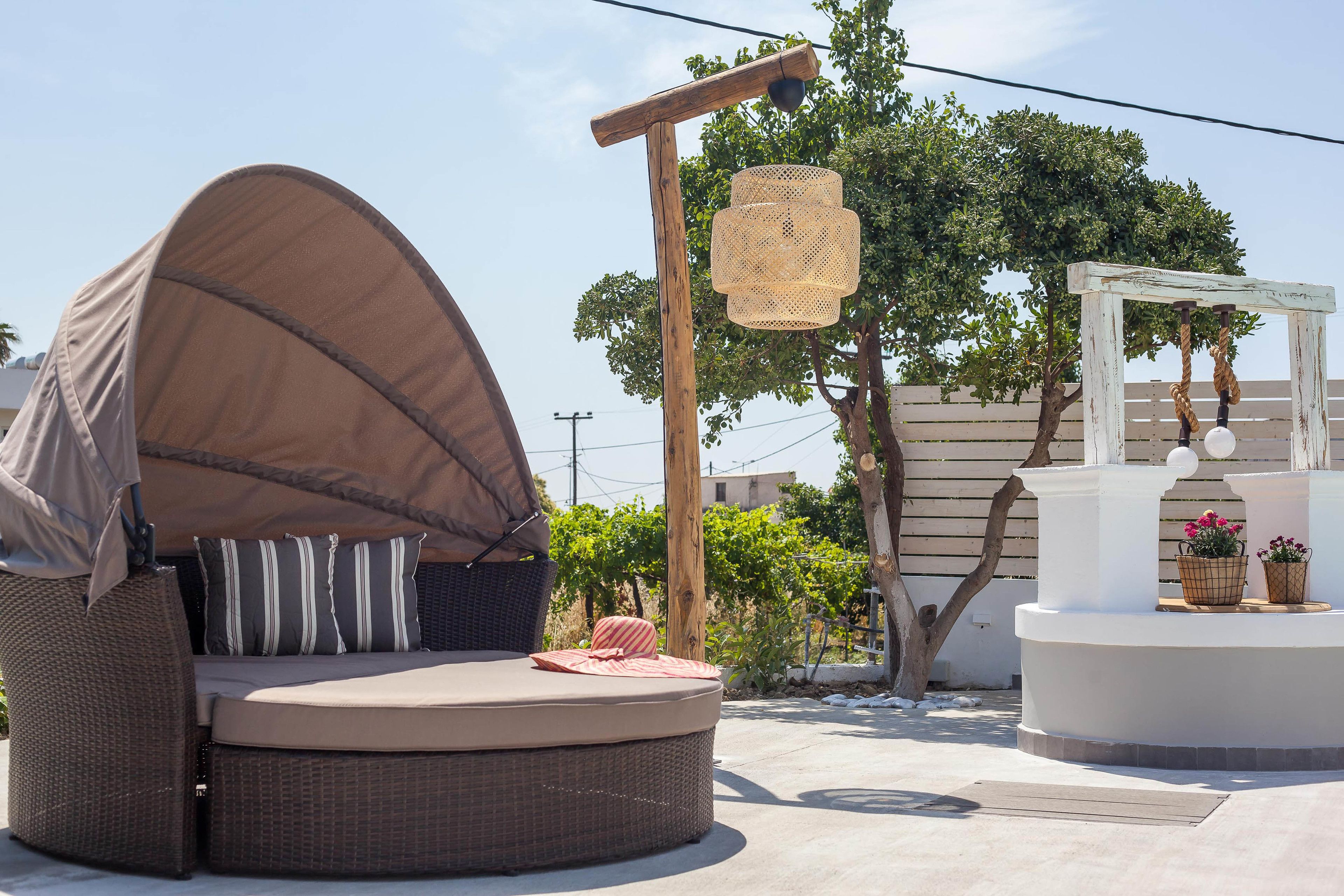 A round outdoor seating area with a canopy, a wooden pergola, and a white structure with plants.