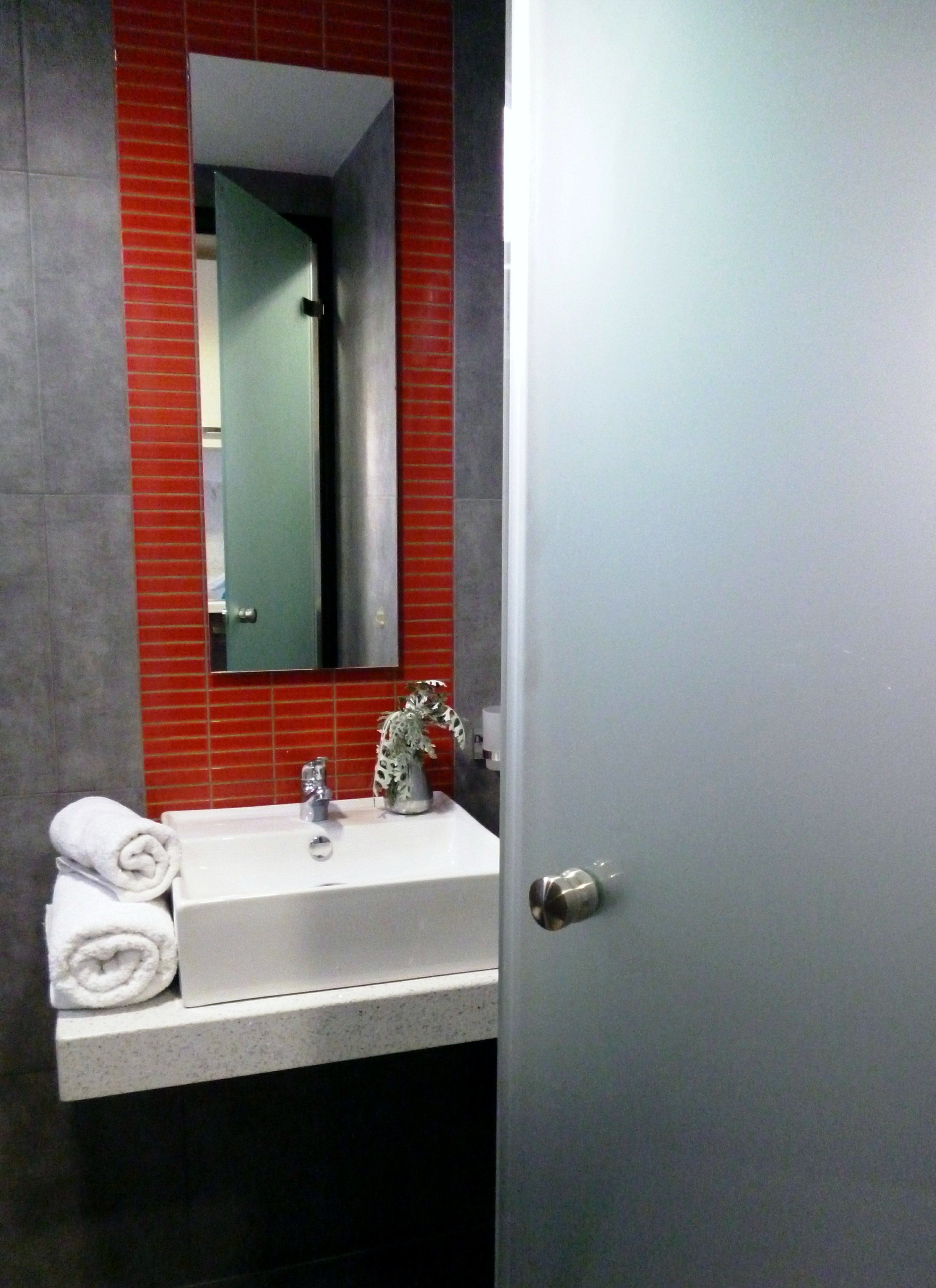 A bathroom with a white sink, a mirror, and a red-tiled wall.