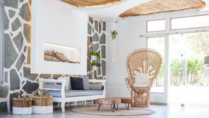 Un salon moderne avec un mur en pierre, un canapé blanc, un fauteuil en osier et une grande fenêtre.