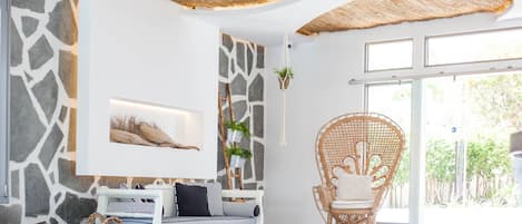 A modern living room with a stone wall, a white sofa, a wicker chair, and a large window.