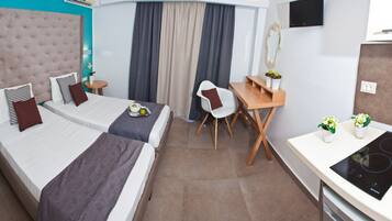 Hotellihuone, jossa on kaksi sänkyä, työpöytä, tuoli, pieni pöytä, televisio ja pieni keittiönurkkaus.