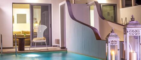 A swimming pool with a curved wall, a chair, and two lit lanterns.