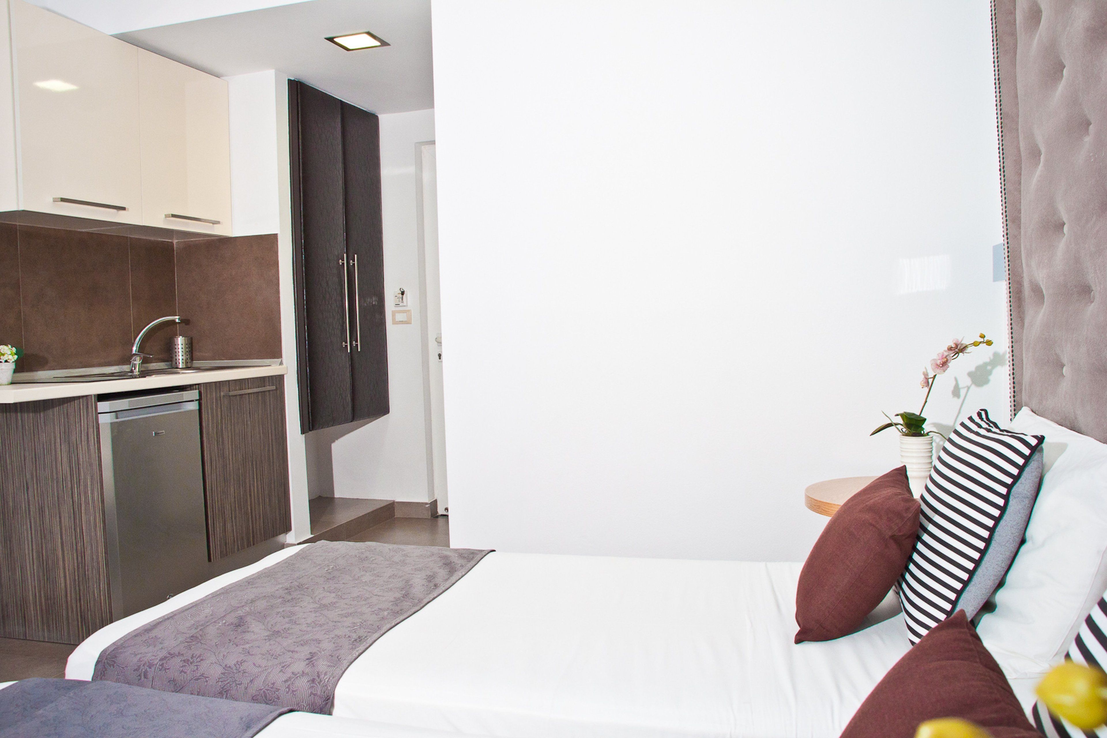 A modern hotel room with a bed, bedside table, and a view of the kitchen.