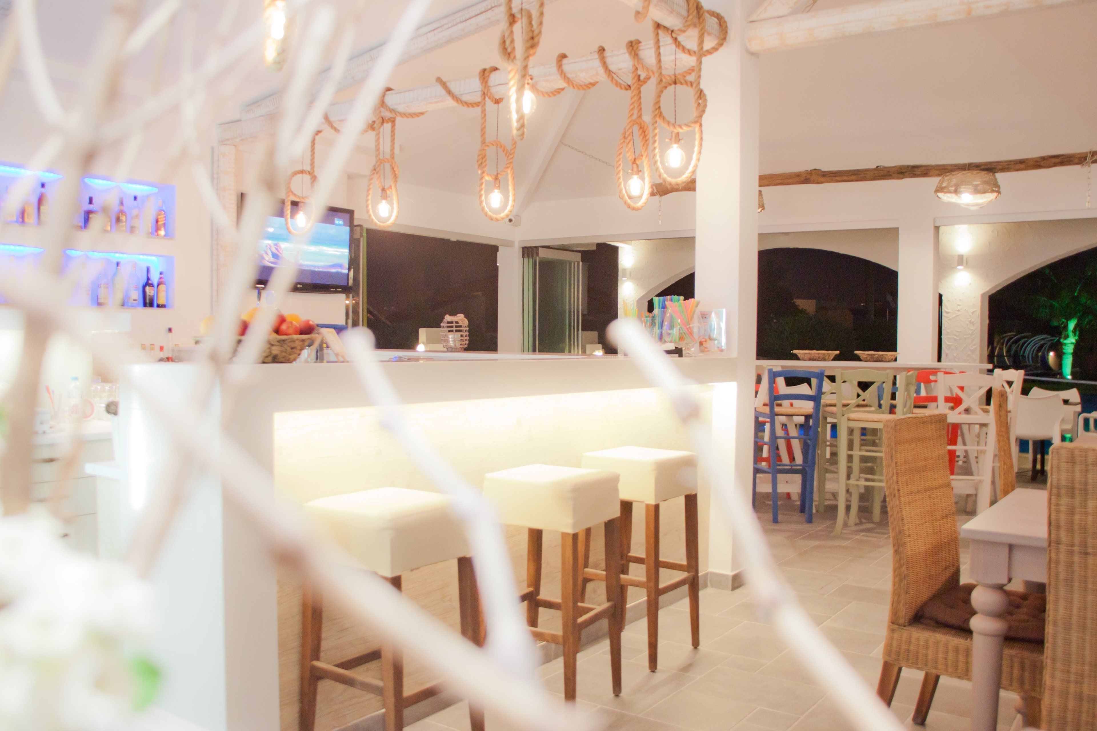 A modern bar area with white bar stools, a counter, and hanging light fixtures.