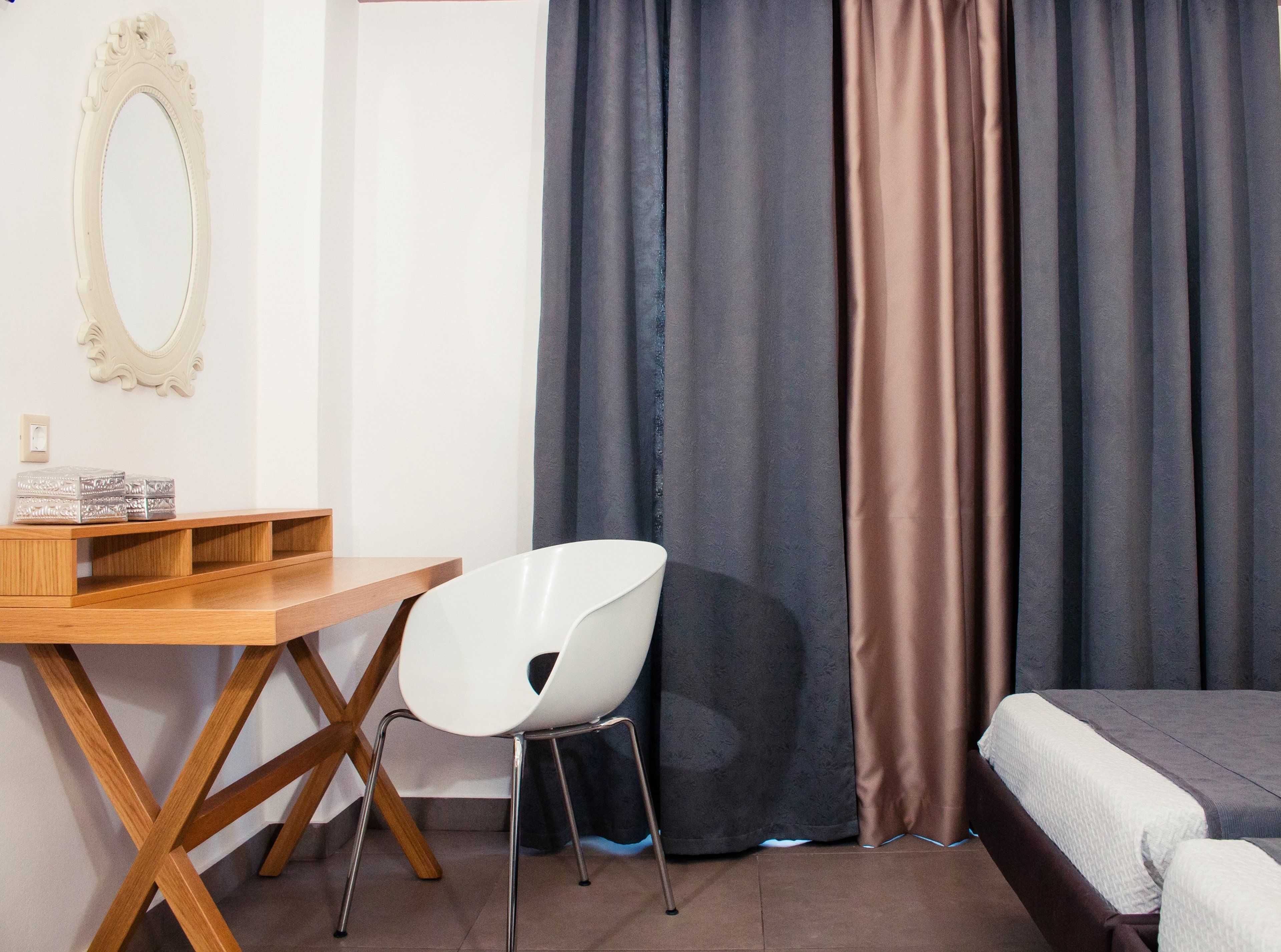 Une pièce avec un bureau en bois, une chaise blanche, un lit et une grande fenêtre avec des rideaux.