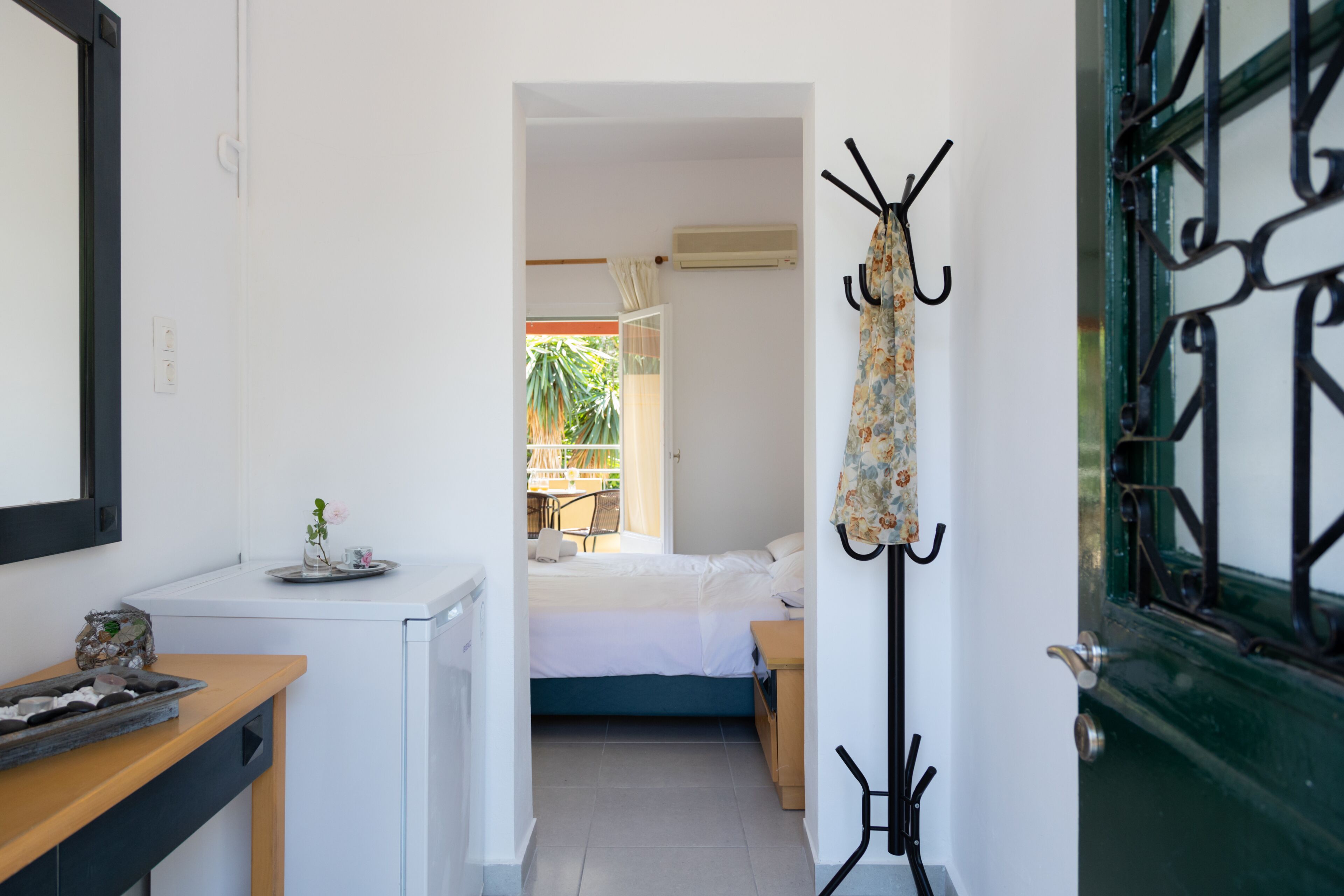 Habitación de hotel pequeña con cama, escritorio, perchero y puerta con una celosía de metal decorativa.