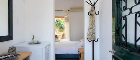Habitación de hotel pequeña con cama, escritorio, perchero y puerta con una celosía de metal decorativa.
