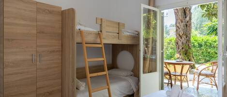 Ein Zimmer mit einem Etagenbett, einem Holzschrank, einer Himmelsleiter, einem Bett mit Handtüchern und Blick auf einen Außenbereich mit Tisch und Stühlen.