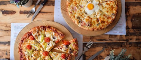 Two pizzas on wooden boards with menus, a knife, and a fork on a wooden table.