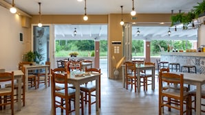 Un restaurant spacieux avec des tables et des chaises en bois, des luminaires suspendus et une vue sur la verdure environnante.