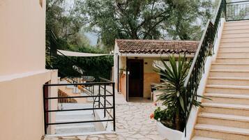 A stone staircase leading to a covered entrance with a tiled roof, surrounded by greenery and trees.