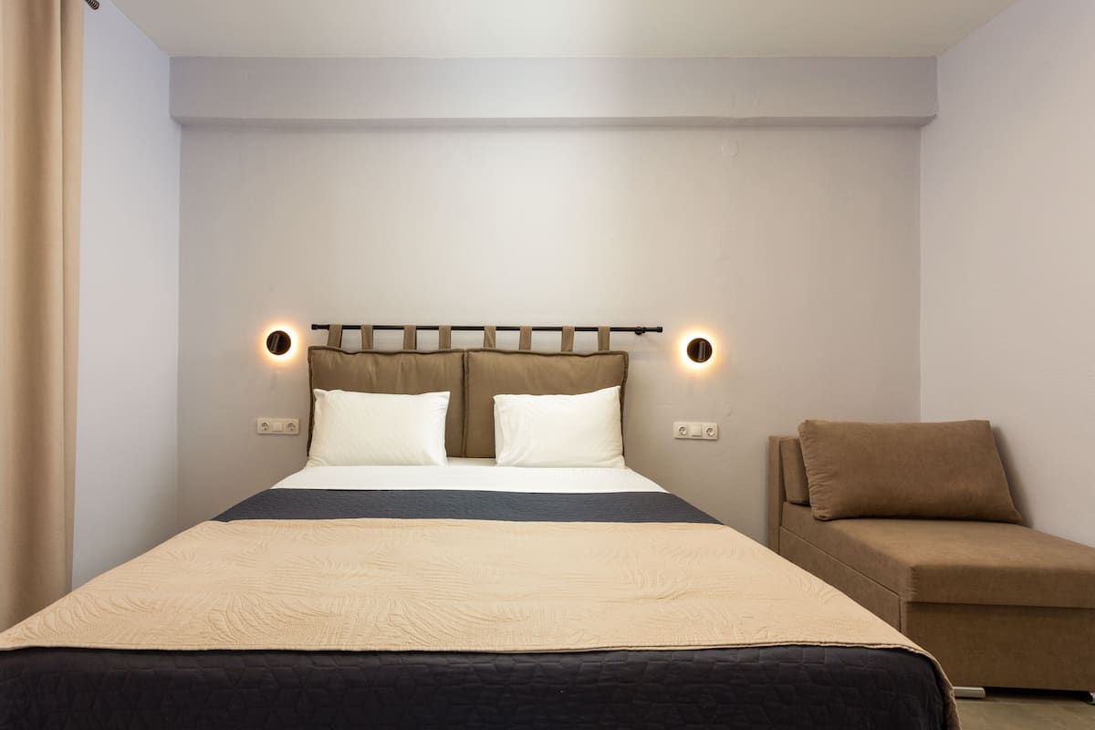A neatly arranged bedroom with a bed, bedside lamps, and a sofa.