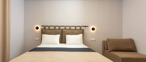 A neatly arranged bedroom with a bed, bedside lamps, and a sofa.