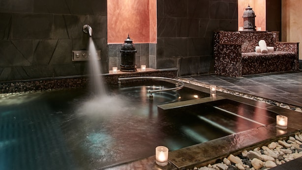 Un área de spa con hidromasaje, pared de piedra, banco de azulejos y velas.