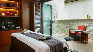 Un cuarto de spa con una camilla de masaje, un espacio de descanso pequeño y vistas al exterior.