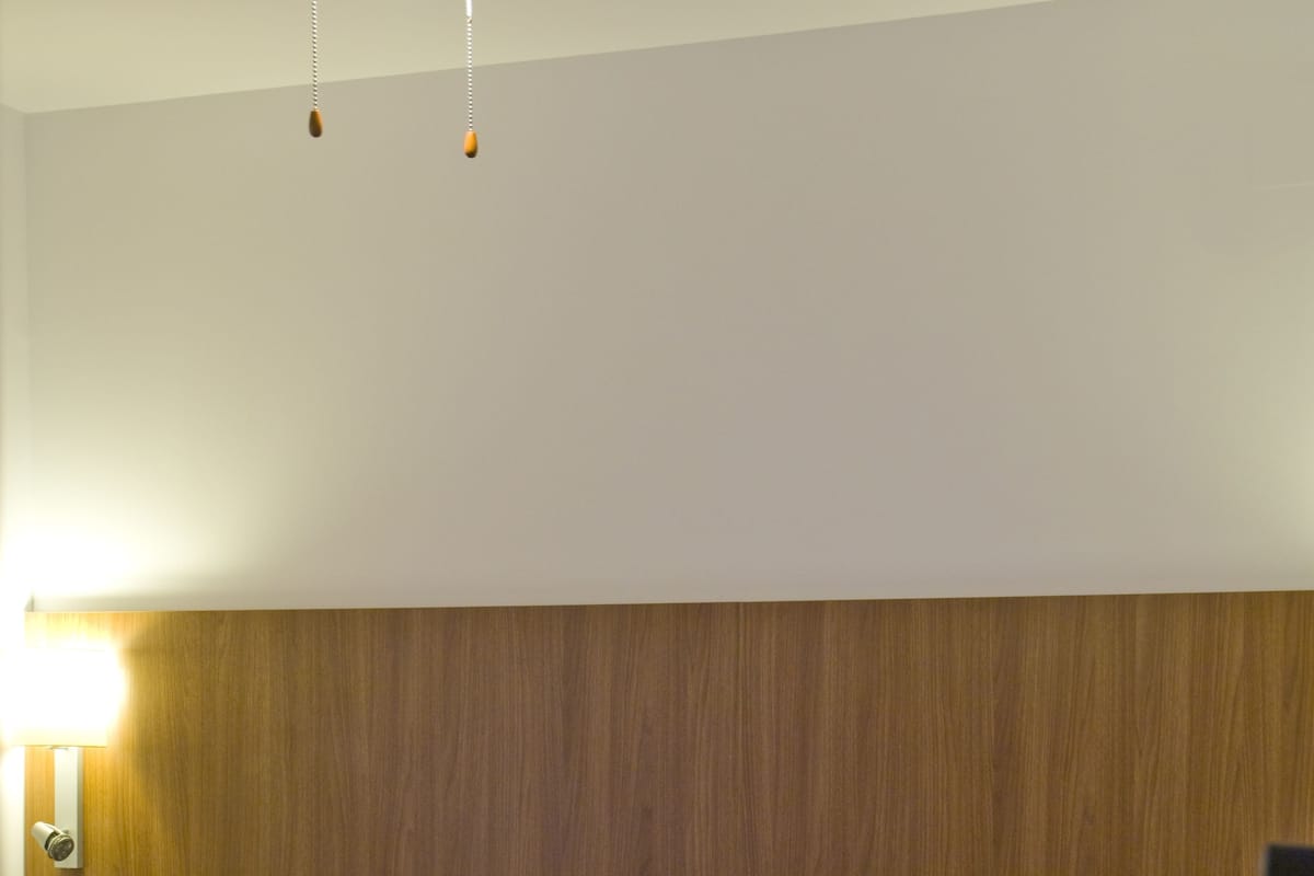 A hotel room with a bed, a ceiling fan, and a wall-mounted light.