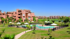 Un resort con piscina, sillas de descanso y un campo de golf al fondo.