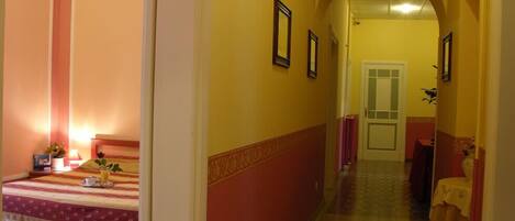 Un pasillo de hotel con una cama a la izquierda, una puerta al final y una mesa con mantel a la derecha.